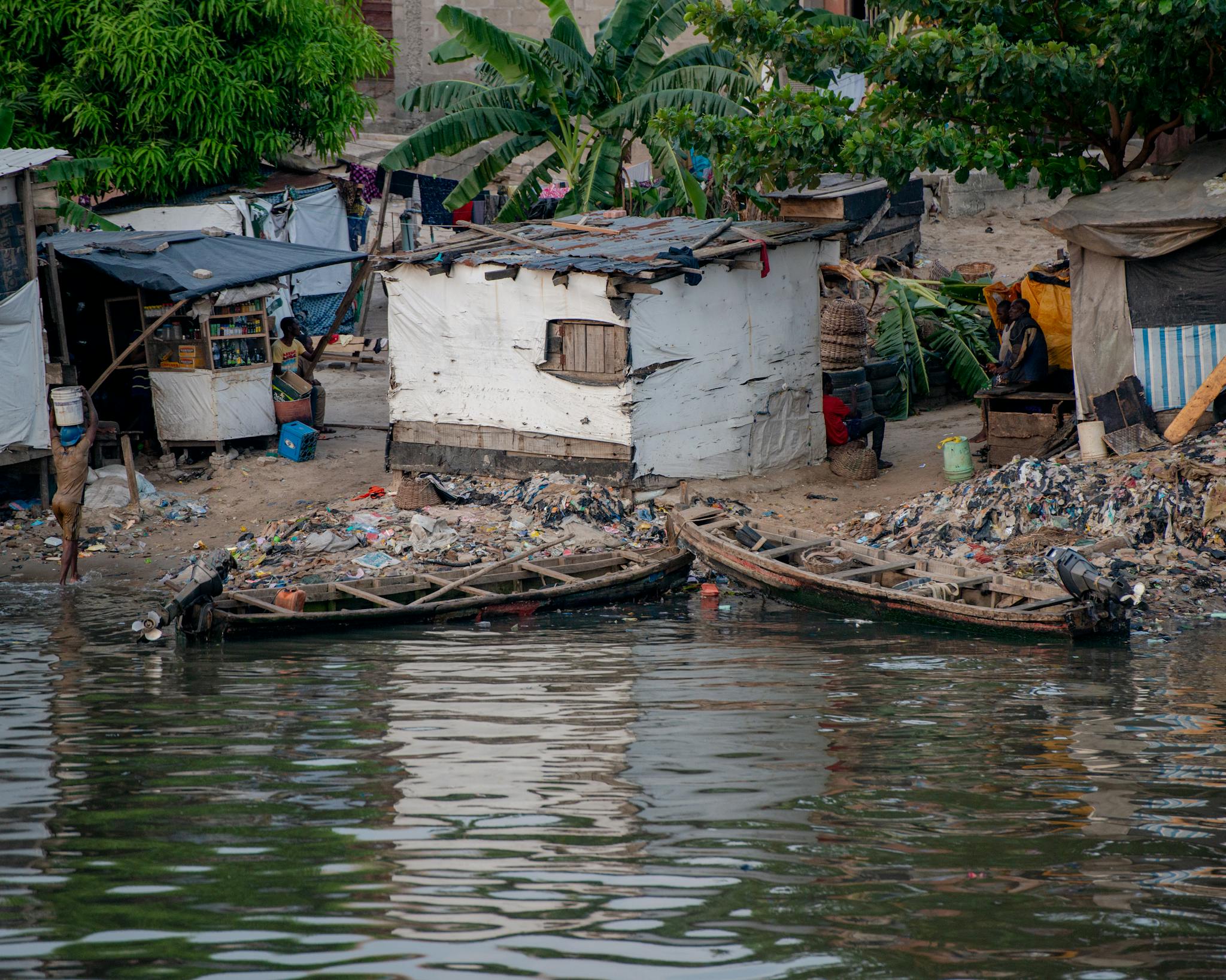 Flooded huts and boats on a littered riverbank in Lagos, Nigeria, depicting urban poverty.